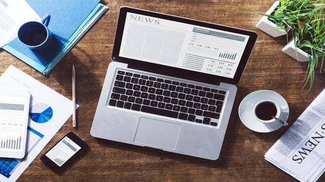 Laptop on office table with current newspaper